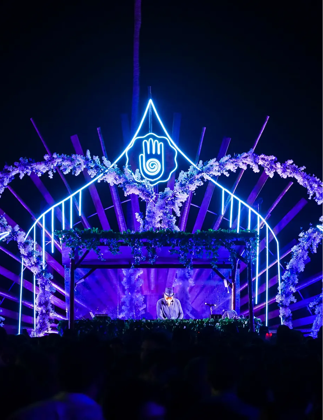 DJ en escenario con arco de luz azul y flores